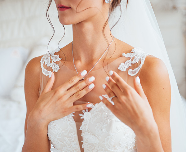 A bride in a white lace wedding dress gently touches her necklace, in California - wedding photography by Leah Marie Photography