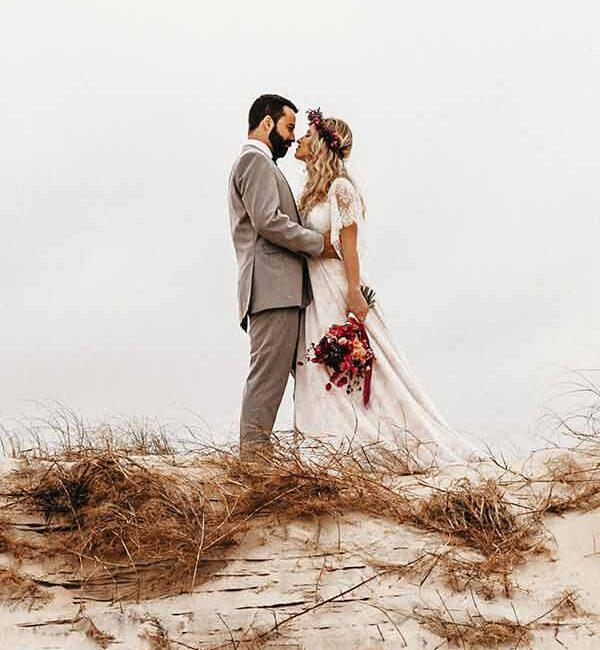 A bride and groom stand on a sandy hill covered with dry grass, in California - wedding photography by Leah Marie Photography