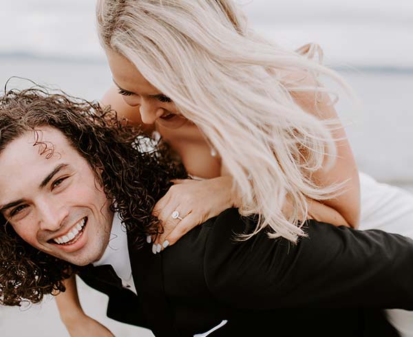 A joyful couple dressed formally, with a woman playfully riding on a mans back, in California - wedding photography by Leah Marie Photography