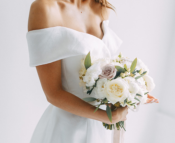 A bride in an off-the-shoulder white wedding dress holds a bouquet, in California - wedding photography by Leah Marie Photography