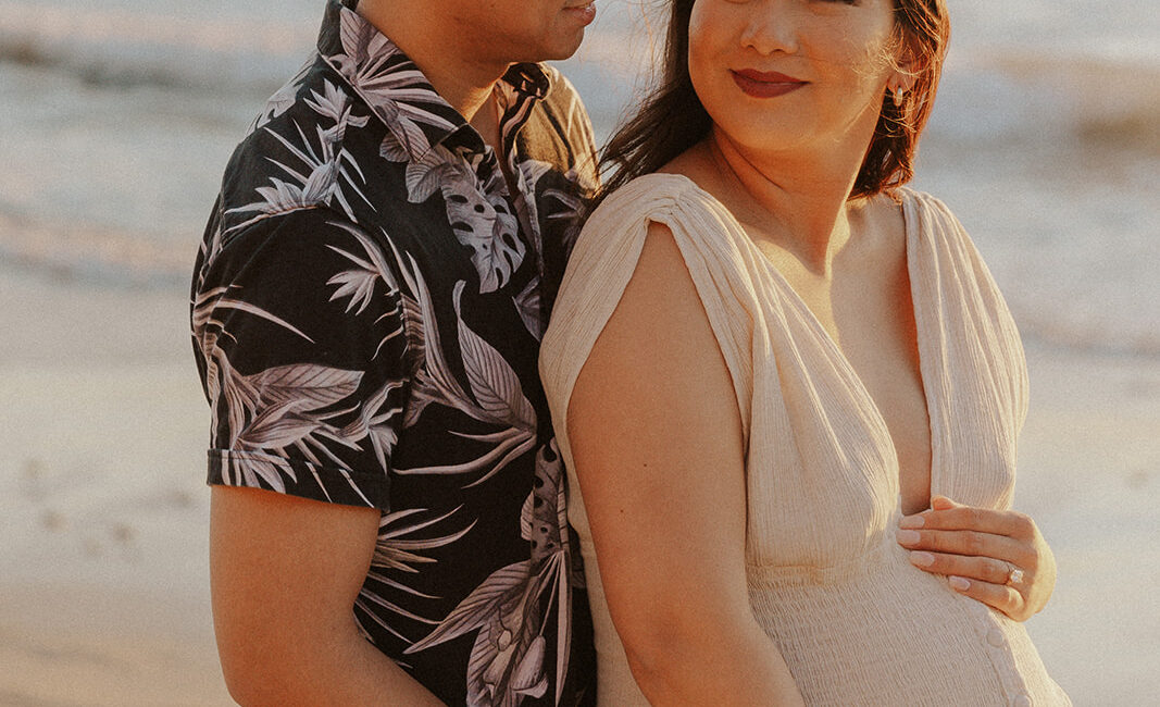 A expectant couple stands on the beach at sunset, in California - portrait photography by Leah Marie Photography