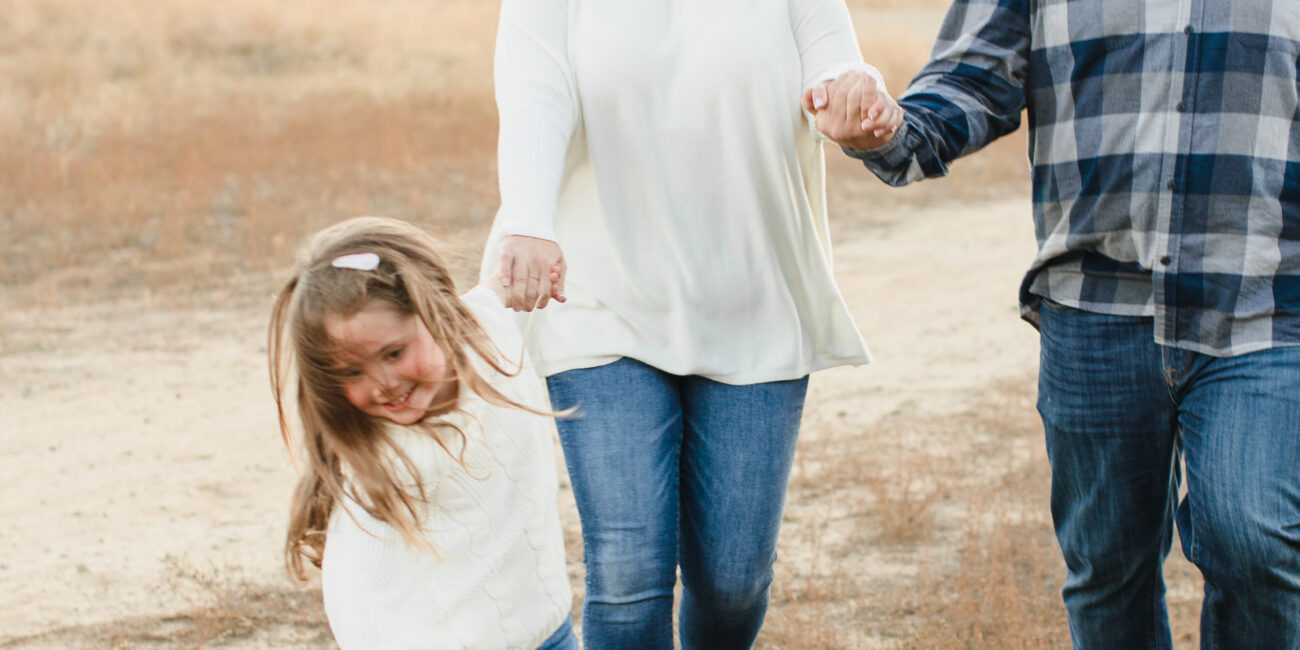 A smiling family of three walks outdoors on a grassy trail, in California - portrait photography by Leah Marie Photography