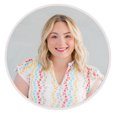 A smiling woman with shoulder-length blonde hair wearing a white blouse with colorful patterns, standing against a light background. Leah Marie Photography - southern california