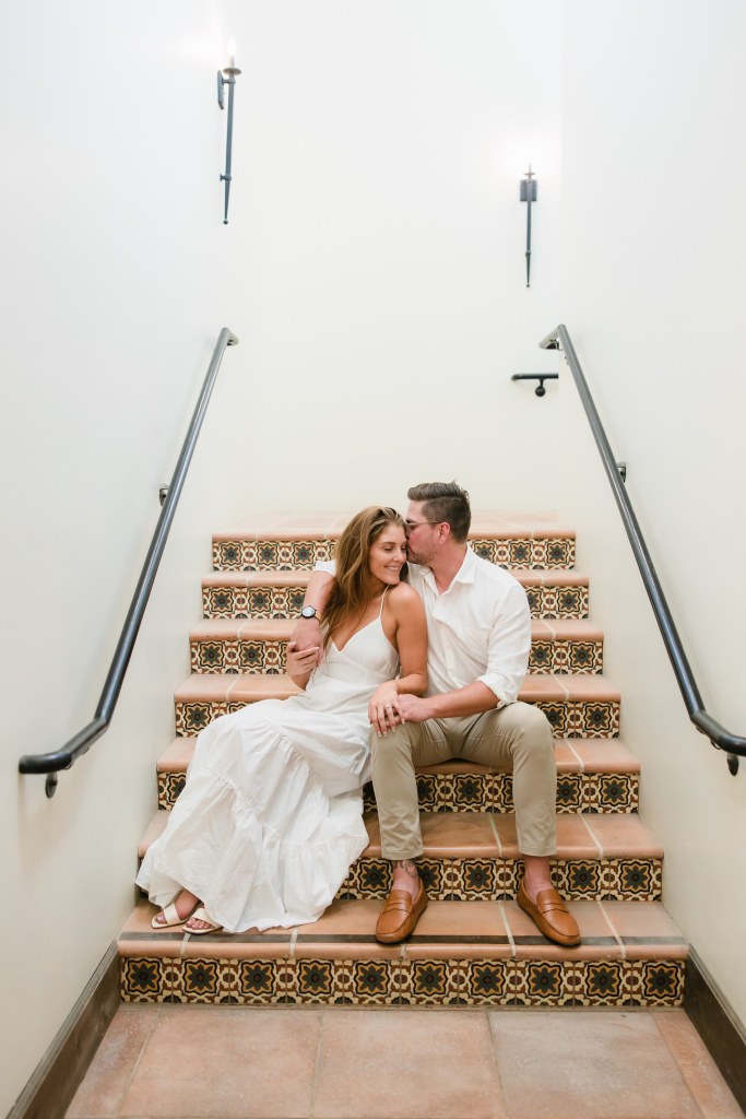 A couple sits on tiled stairs, holding hands and leaning close at Europa Village in Temecula, California - engagement photography by Leah Marie Photography
